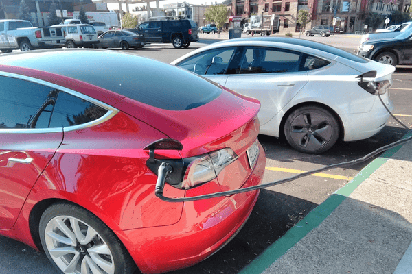 Photo of a red and white Tesla parked and plugged in to a charger.