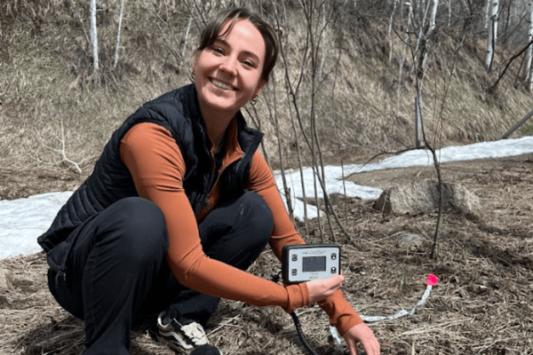 Image of a person crouched down smiling with a soil sampling device.