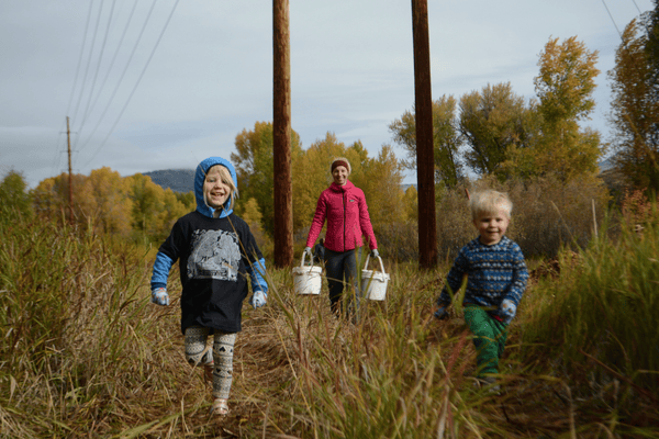 Image of two kids running the grass with adult holding buckets in background.