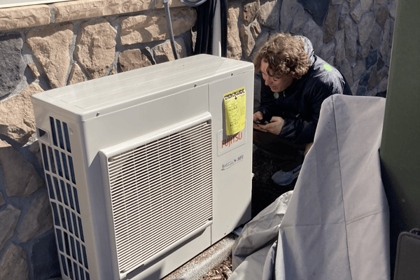 Image of a young man crouching down near a heat pump.