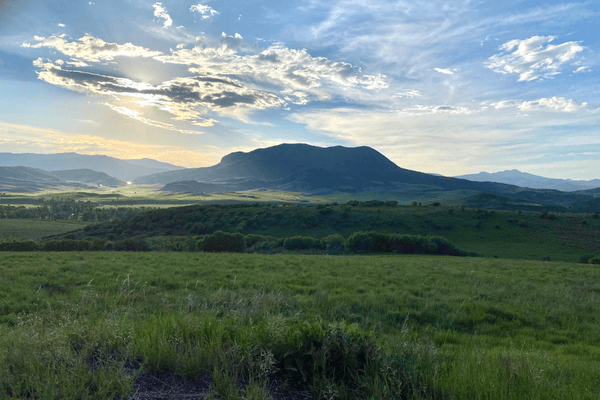 Image of a mountain with green grass field in the foreground.